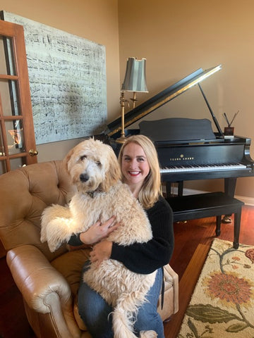Sarah Alonso, Chief Marketing Officer of The Bold Bow Tie, sits in a formal living room in front of a piano with her golden labradoodle puppy, George. 