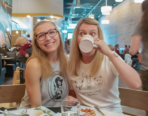 Two women sitting together at a table, sipping coffee and conversing warmly.