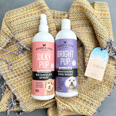 Silky Pup Detangler Spray and Bright Pup Dog Wash bottles lying on tan Solwoven Towel
