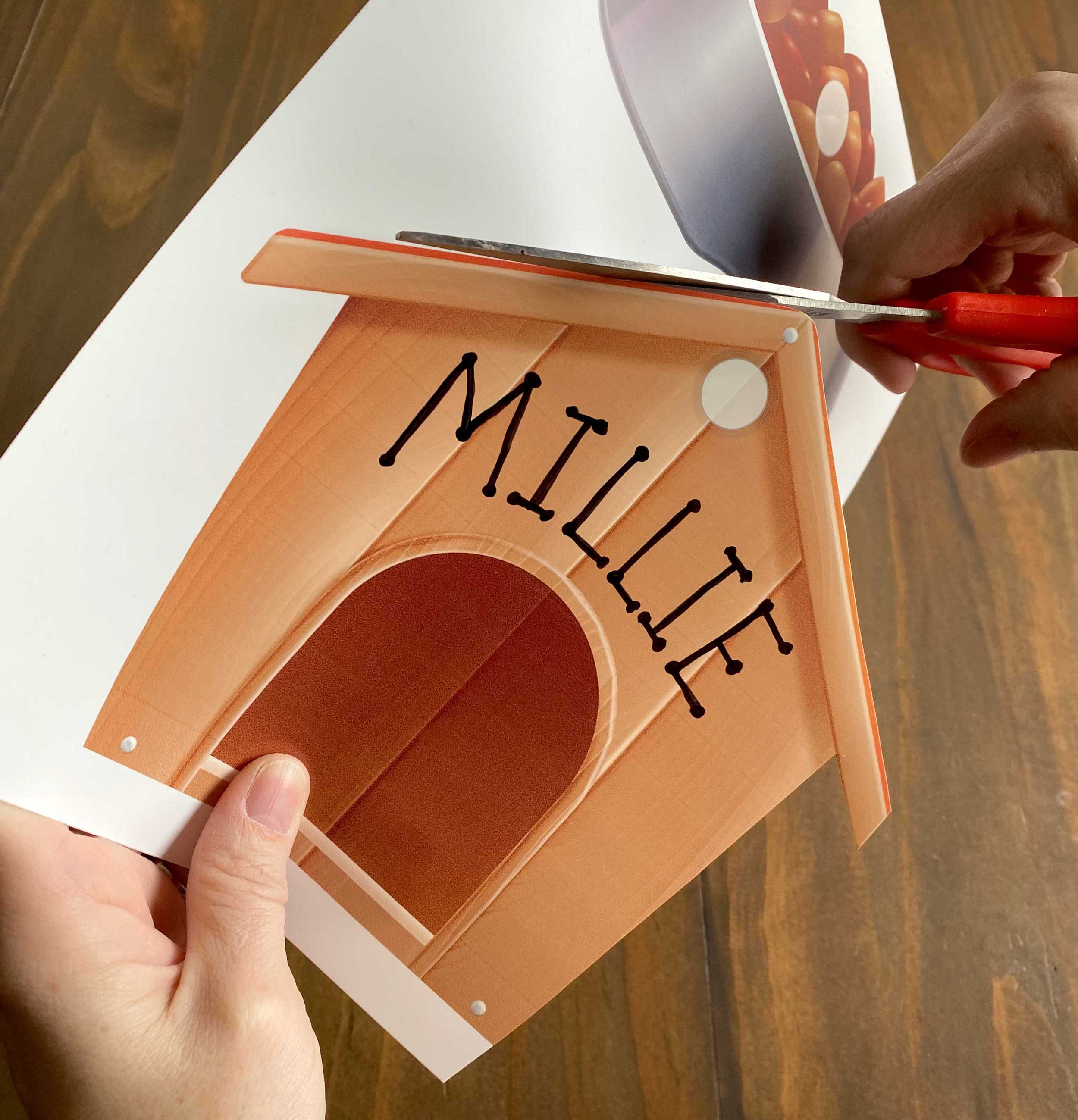 hand cutting out doghouse with the name Millie written on it