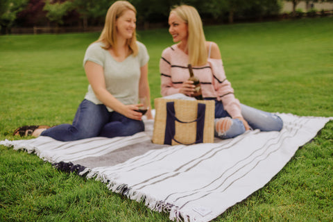 two women sitting on a picnic blanket with a willow picnic basket and bottle of wine