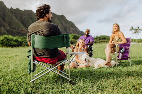 man sitting on a sports chair talking to two friends sititng across from him with a dog on the ground