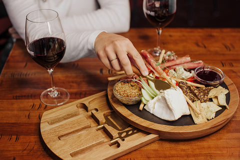 man slicing cheese on a cheese board with tools and a slate top