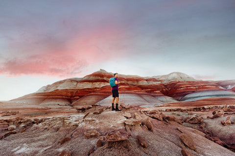 man hiking bentonite hills while holding blue backpack made from recycled materials