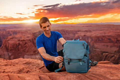 man hiking horseshoe bend while holding blue backpack made from recycled materials