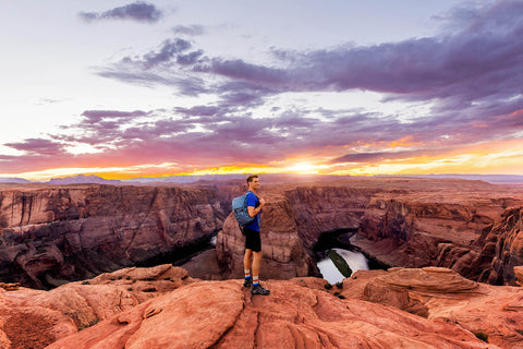 man hiking horseshoe bend while holding blue backpack made from recycled materials