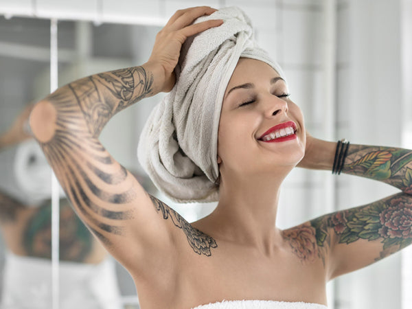 smiling girl with colorful tattoos stands with closed eyes in the bathroom