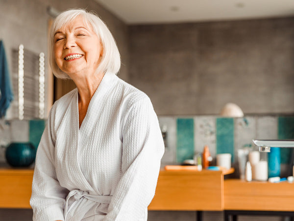 Smiling senior lady in bathrobe sitting on the edge of bathtub
