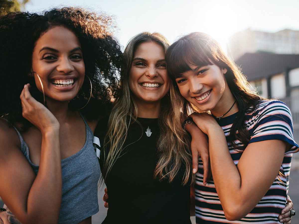 A group of three women outside, embracing, smiling at the camera.