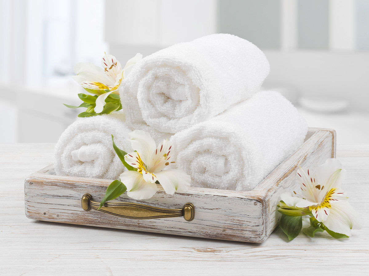  A tray holding three rolled white towels resting on a counter in a spacious white bathroom.