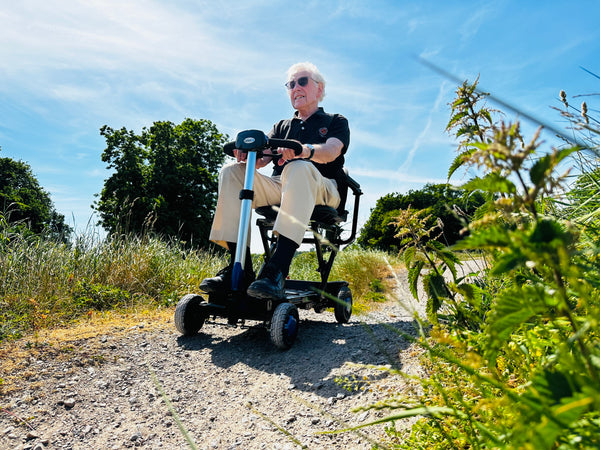 A man riding a Zinnia Carbonlite folding mobility scooter along a gravel path