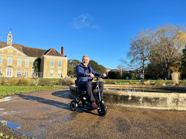 A man on a scooter glides gracefully in front of a beautiful fountain, enjoying the serene surroundings.