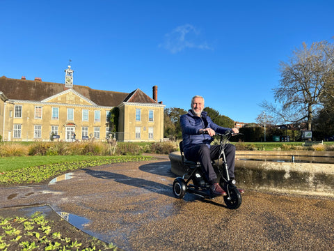 A man riding a folding mobility scooter on a wet pavement in a park