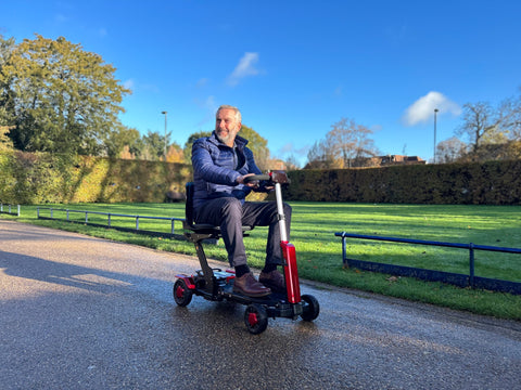 A man riding a bettyandbertie Zinnia X folding mobility scooter through a park