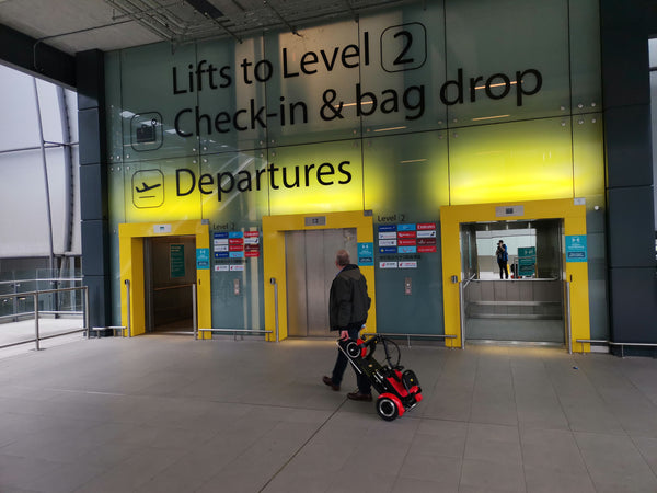 A man pulling a folding mobility scooter through an airport terminal.