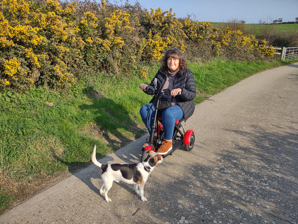 A woman riding her folding mobility scooter along a country lane.