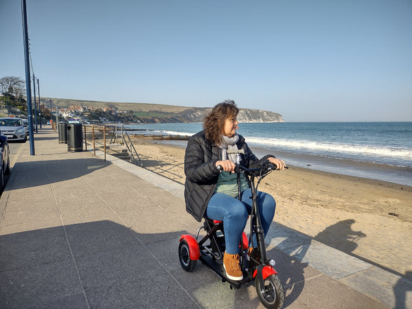 Woman enjoying a ride on a folding mobility scooter along the sandy beach.