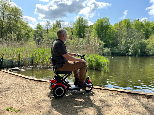 A man enjoying a folding mobility scooter ride next to a peaceful lake.