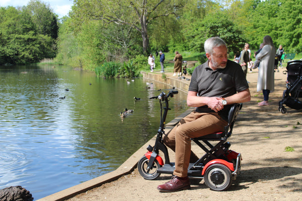 A man on a Lupin Folding mobility scooter at a park.