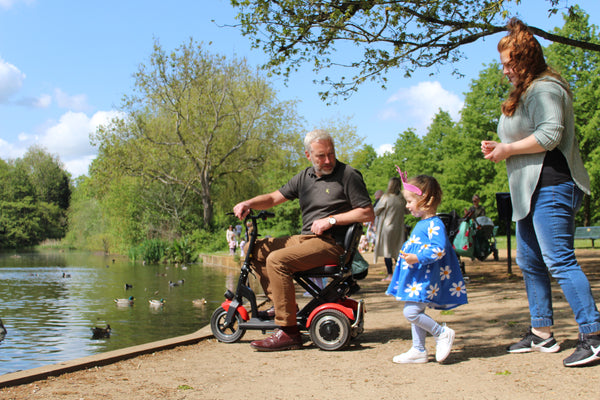 A man on a Lupin folding mobility scooter at a park with family