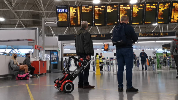 A man pulling a folding mobility scooter through a train station.