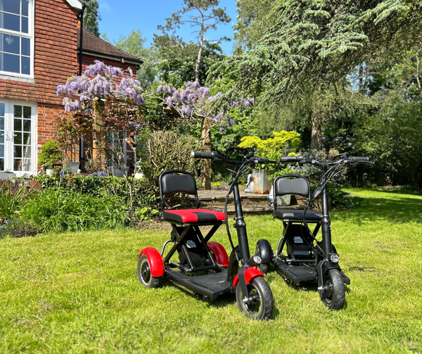 Two electric scooters parked in front of a house - the Lupin and Ren folding mobility scooters by Betty and Bertie Mobility.