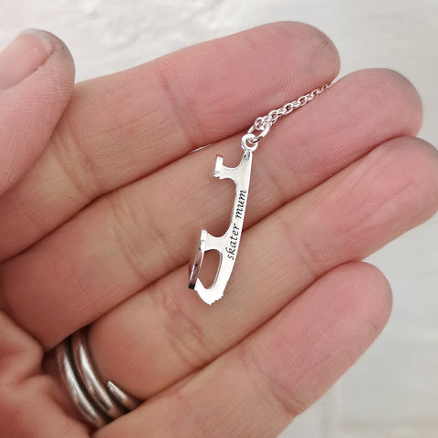hand holding a silver ice skating necklace engraved with the words skater mum
