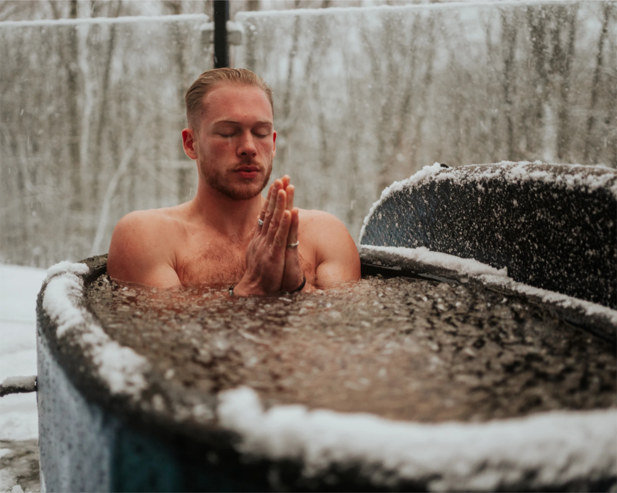 Person meditating in an outdoor ice bath surrounded by snow.