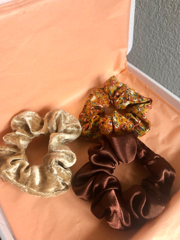 Three mini scrunchies - one is good velvet, one is brown satin, and the third one is orange and neutral toned micro floral.