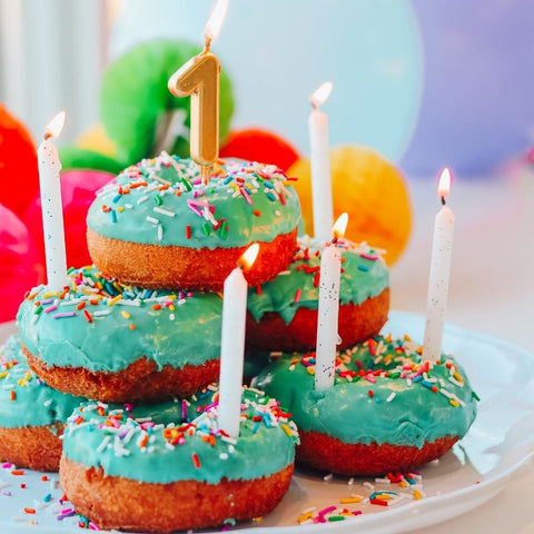 A stack of doughnuts with aqua icing and colorful sprinkles fitted with lit candles