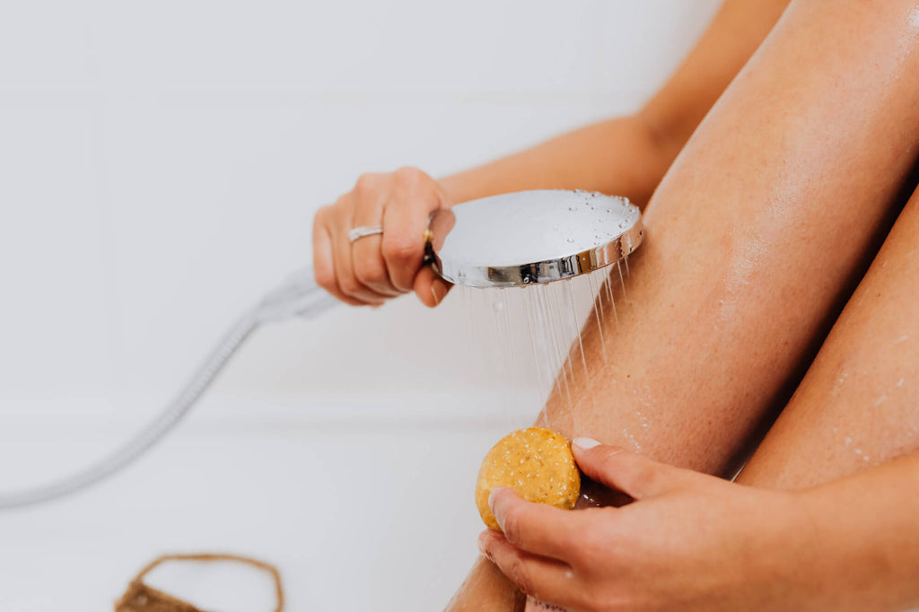 Miljøbilde av kvinne med dusjhode og skrubb som rengjør bena. Benyttes i blogginnlegget Hvordan fjerne kalk fra dusjhodet