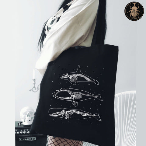 A girl holding a black goth tote bag with whale skeletons design on it.