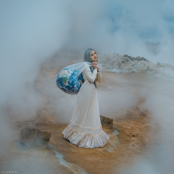 an Anya Anti photograph of a young woman in a white dress holding a melting globe surrounded by fog