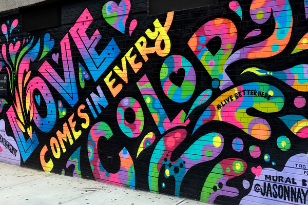 a mural that says "love comes in every color" by NYC based artist Jason Naylor, in anticipation of his upcoming collaboration with Patricia Barrett Studio for Pride Month NYC 2022