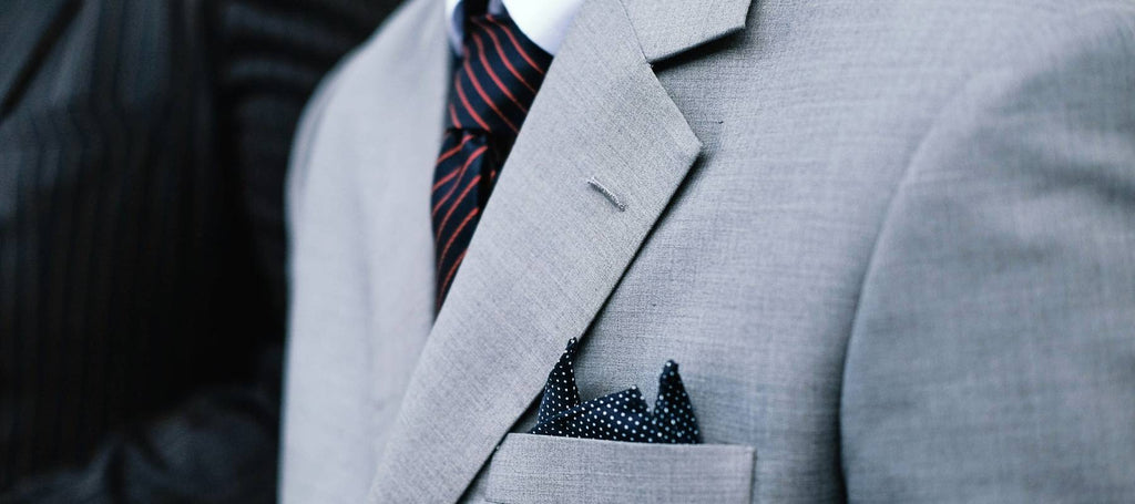 Traje gris, corbata negra y roja y bolso de mano negro con lunares blancos
