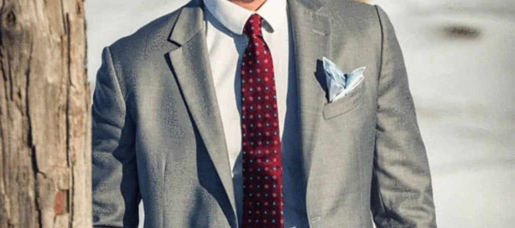 Traje gris claro, corbata roja y clutch plateado