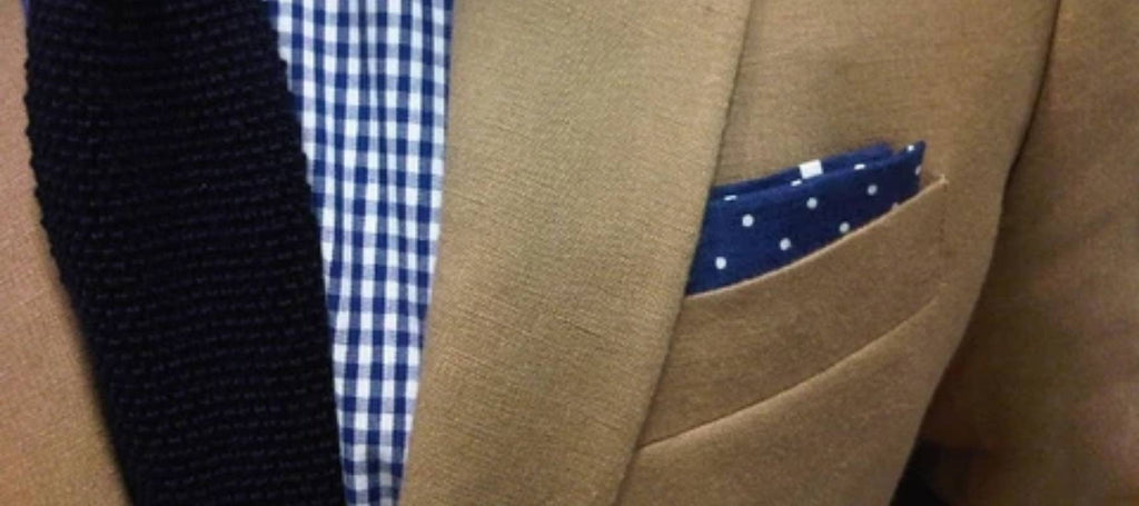 Corbata lisa y pañuelo de bolsillo en azul marino con lunares blancos sobre traje marrón