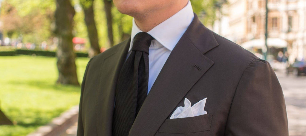 Ein Mann im Freien, der einen schwarzen Anzug und eine braune Krawatte trägt