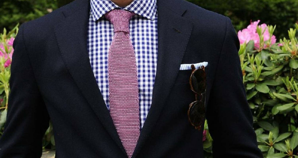 ¿Con qué combinar una corbata de punto? aCorbata de punto rosa con traje azul marino, camisa de cuadros y gafas de sol