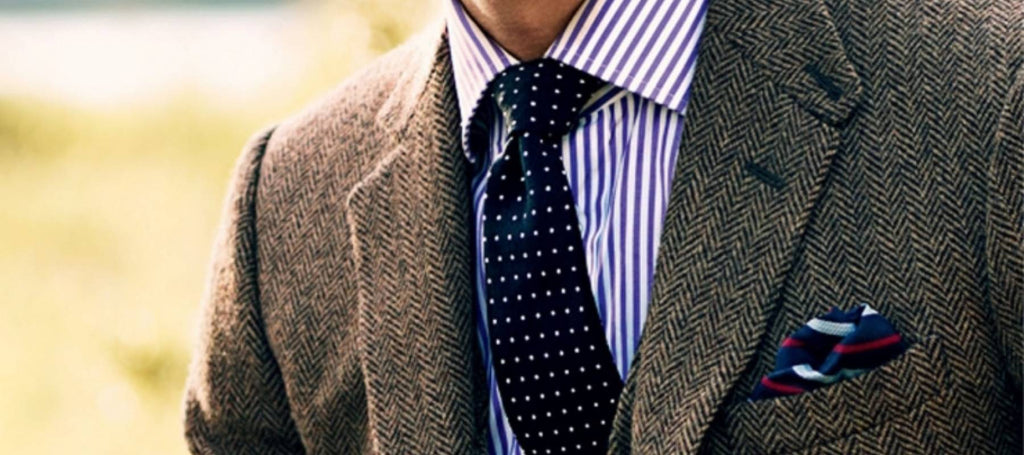Hombre con traje marrón, camisa blanca con rayas azules y corbata blanca de lunares