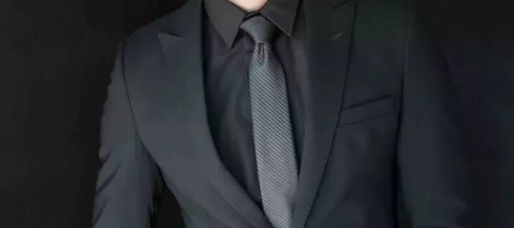 Hombre con traje negro, camisa negra y corbata gris oscuro