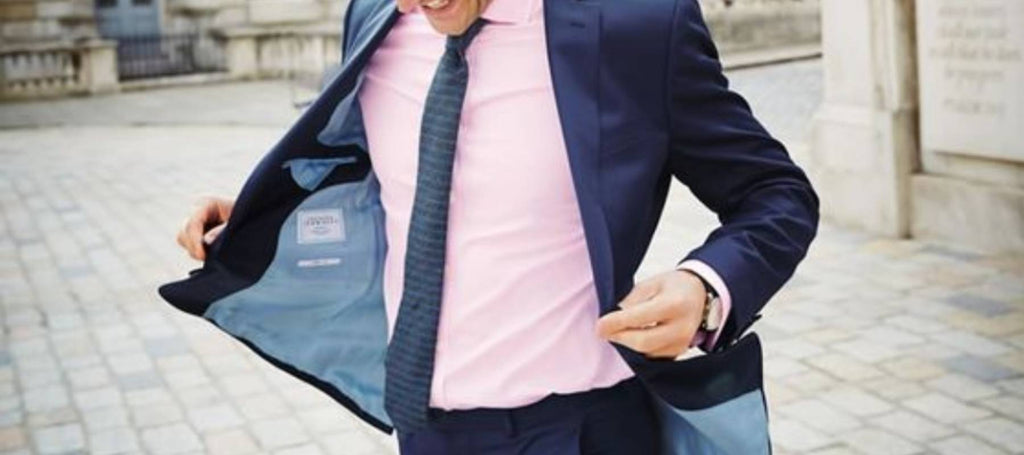 Ein Mann im Freien, der eine marineblaue Krawatte, ein rosa Hemd und einen schwarzen Anzug trägt 