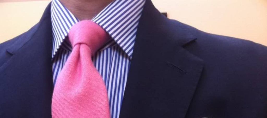 Ein Mann, der ein gestreiftes Hemd, einen schwarzen Anzug und eine rosa Krawatte trägt