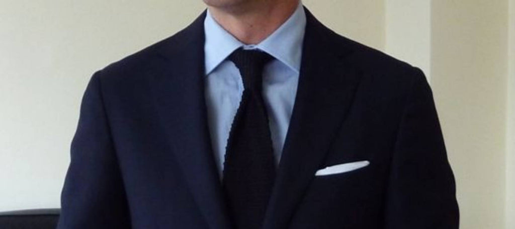 Un hombre con corbata negra, camisa azul y traje negro