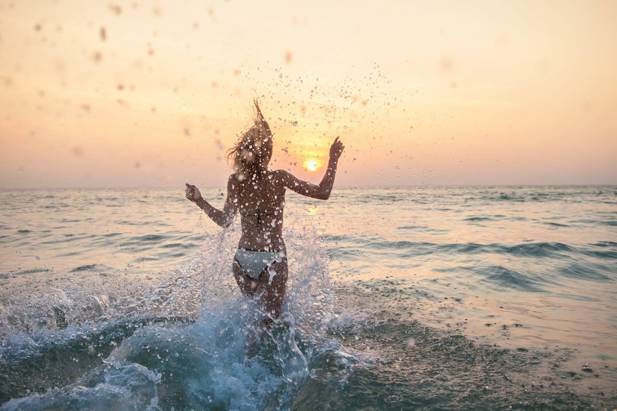 A woman runs into the sea, splashing and having fun as the sun sets.