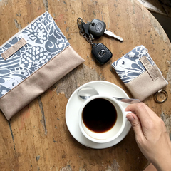 Hand holding coffee cup and on table have batik zip pouch and card holder in grey peony, handcrafted in Malaysia.