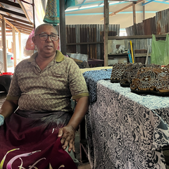 a batik artisan sitting next to batik blocks