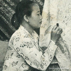 In the vintage photograph, a woman is intricately engaged in the traditional craft of batik-making