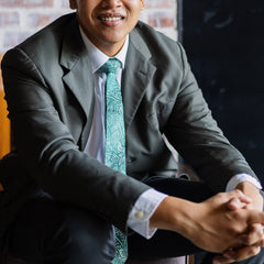 A photo captures a gentleman dressed in formal or corporate attire, seated and elegantly accessorized with a batik tie that complements his outfit