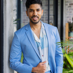 A man strikes a pose in a sharp blue corporate suit, enhancing his professional look with the addition of an authentic batik shirt for a touch of distinct style